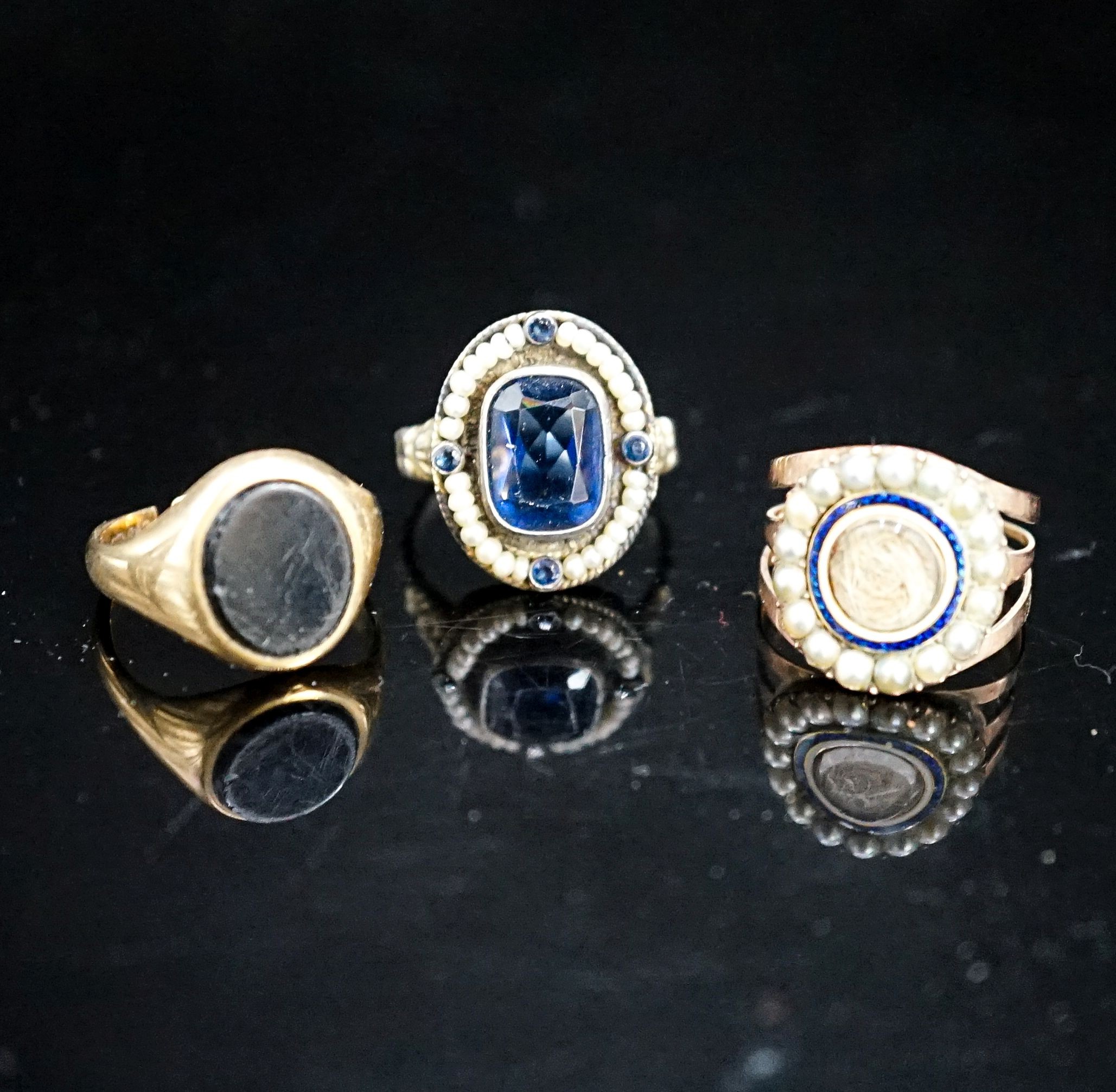 A 19th century yellow metal, two colour enamel and seed pearl set mourning ring, with hair beneath a glazed panel, size N, a 19th century Austro-Hungarian white metal and blue paste ring and a later 9ct gold signet ring(